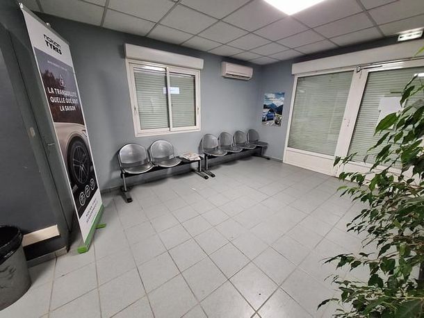 Salle d'attente avec chaises grises, fenêtres et banderole.