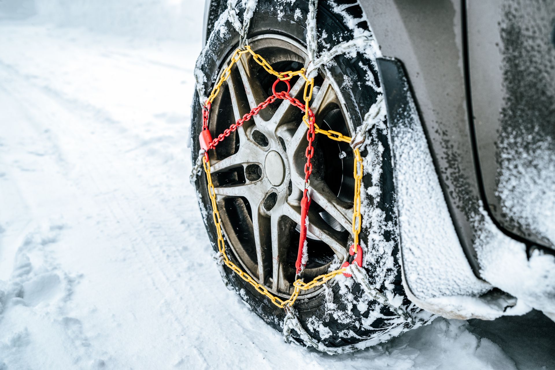 Un pneu de voiture équipé de chaînes à neige sur une route enneigée.