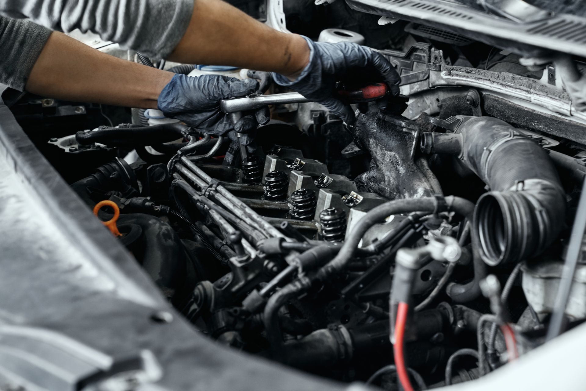 Des mains gantées travaillent sur un moteur de voiture, à l'aide d'outils.