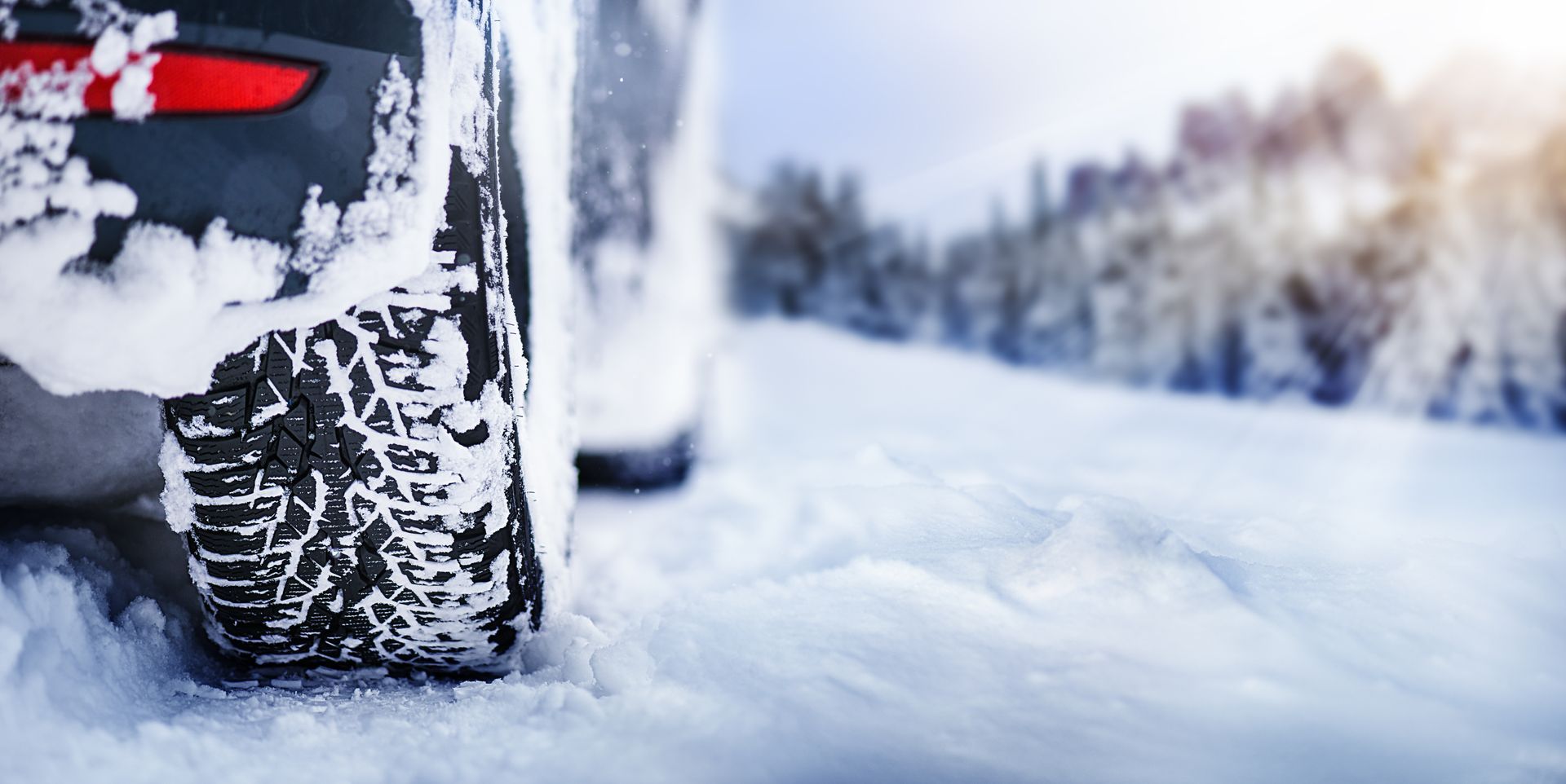 Des pneus de voiture roulent dans une épaisse couche de neige sur une route enneigée, avec une forêt en arrière-plan.