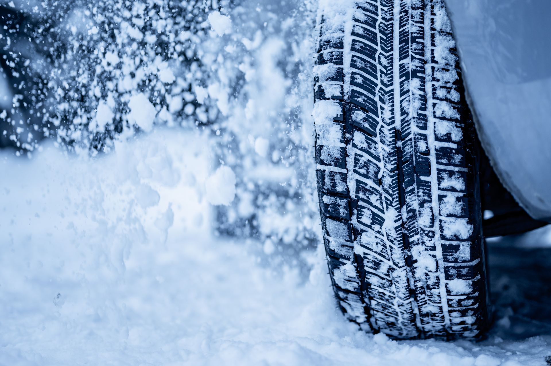 Un pneu de voiture roule dans la neige, soulevant une gerbe de flocons blancs.
