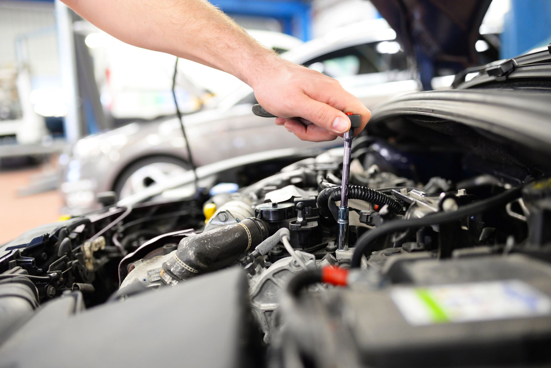 Main d'un mécanicien utilisant un outil pour travailler sur un moteur de voiture dans un garage.