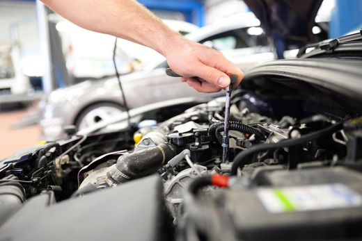 Main d'un mécanicien utilisant un outil pour travailler sur un moteur de voiture dans un garage.