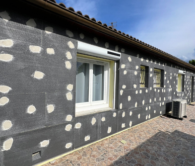 Extérieur de la maison avec isolation foncée, taches d'adhésif de couleur claire et une fenêtre blanche.