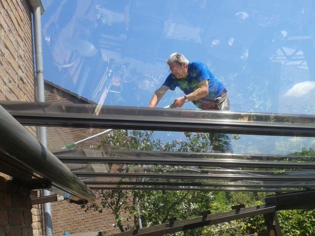 Ein Mann reinigt ein Glasdach mit einer Bürste.
