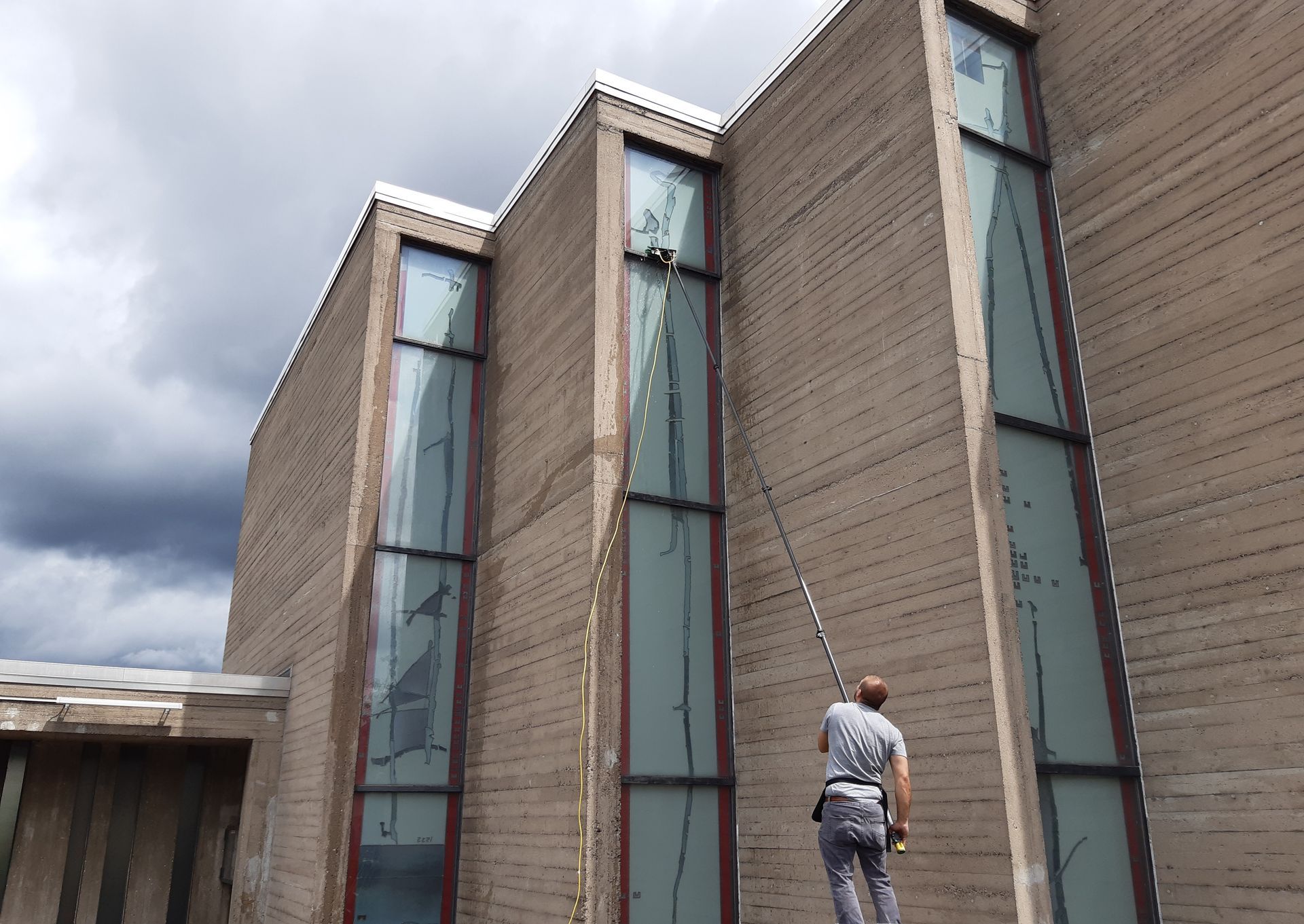 Ein Mann putzt mit einem Schlauch die Fenster eines Gebäudes.
