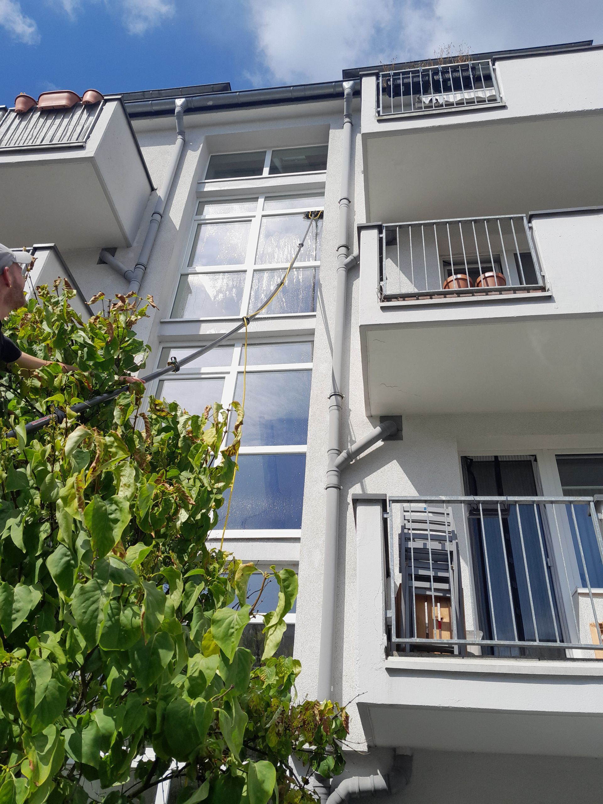Ein Mann putzt mit einem Schlauch die Fenster eines Gebäudes.
