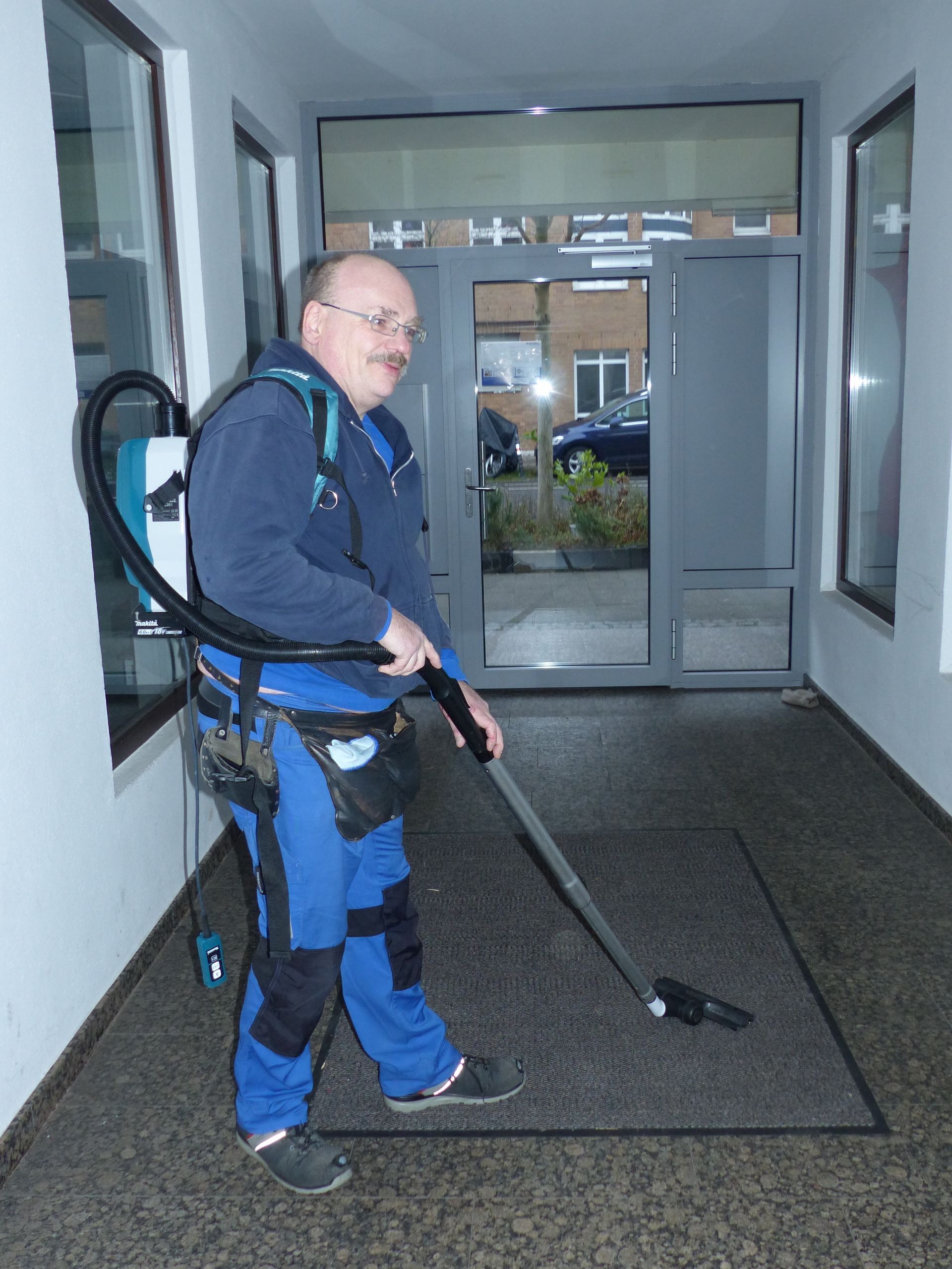 Ein Mann reinigt einen Flur mit einem Rucksackstaubsauger