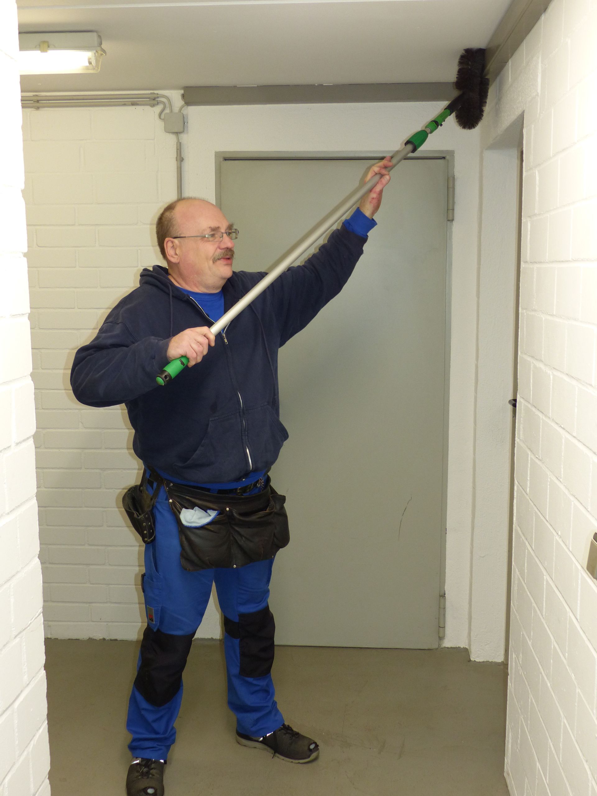 Ein Mann in einer blauen Jacke hält einen langen Besen