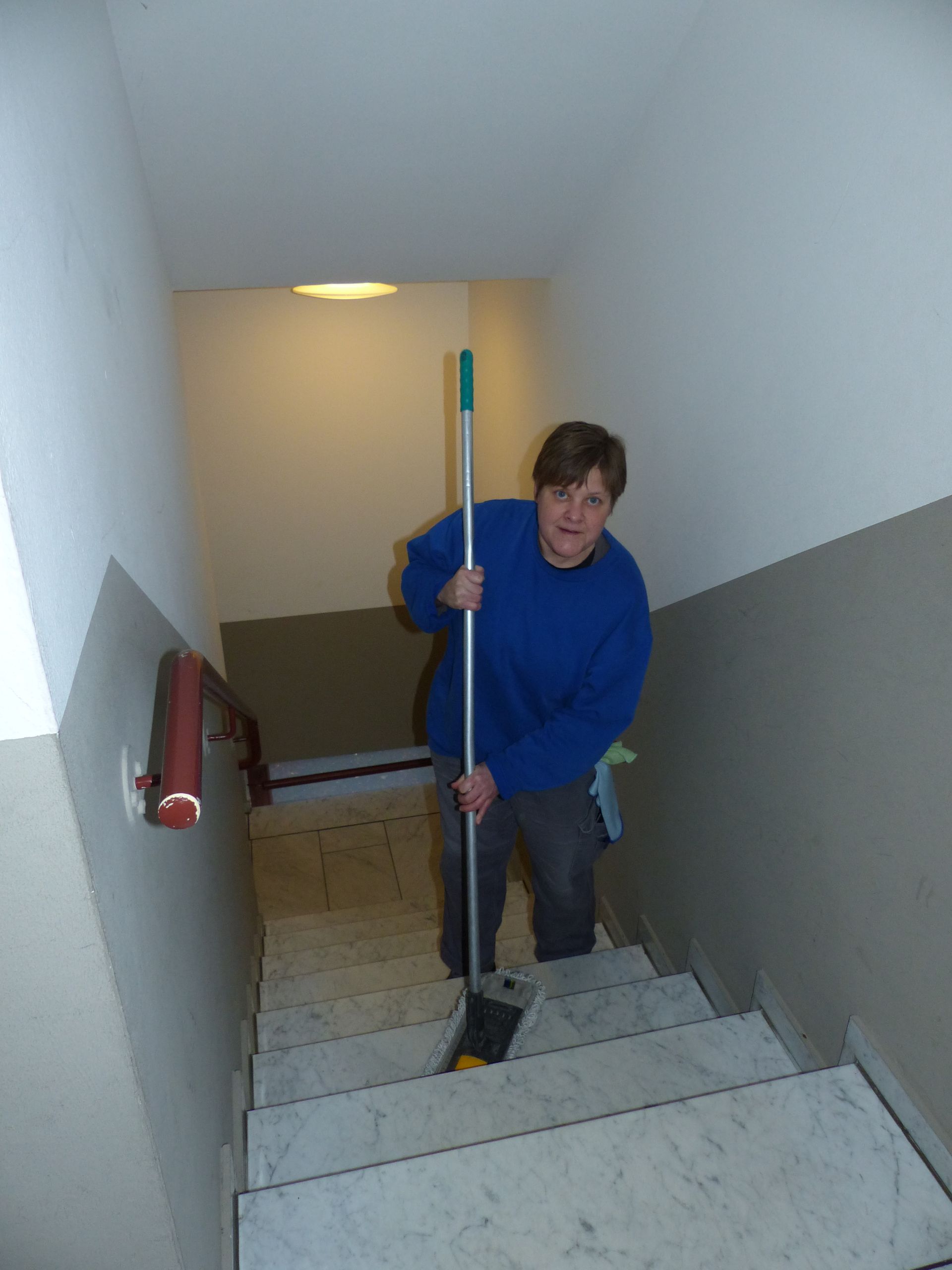 Ein Mann im blauen Pullover putzt die Treppe mit einem Wischmopp