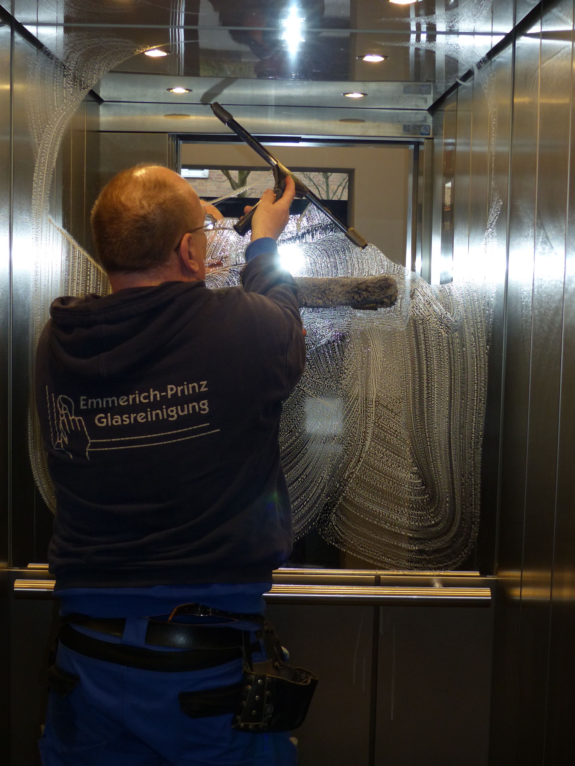 Ein Mann reinigt das Innere eines Aufzugs mit einem Besen.