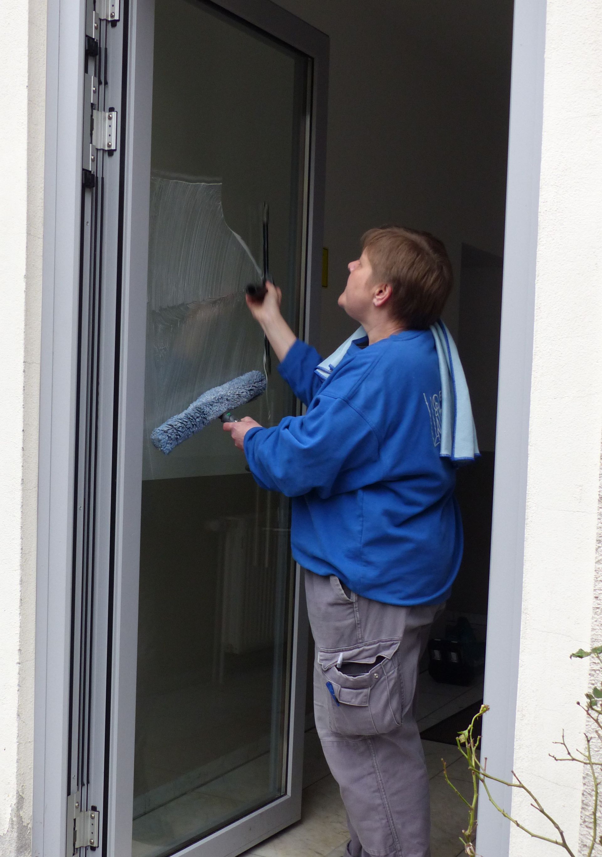 Eine Frau im blauen Hemd putzt eine Glastür