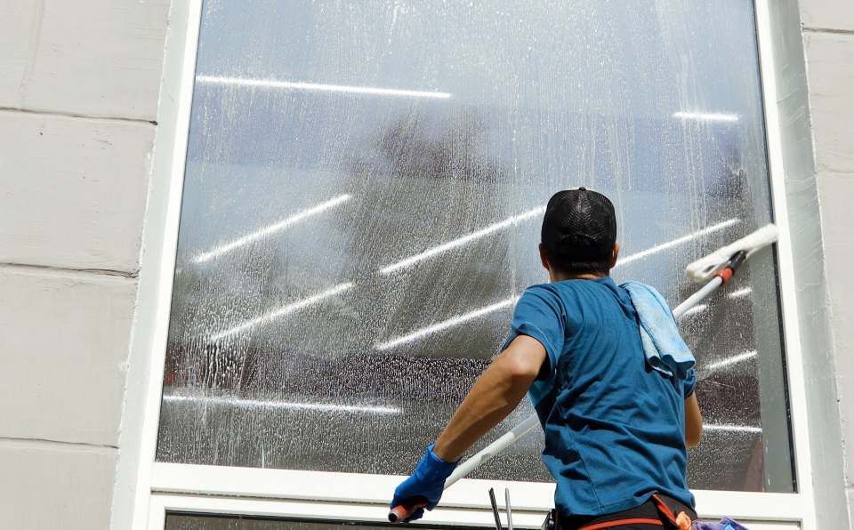Ein Mann putzt ein Fenster mit einem Abzieher.