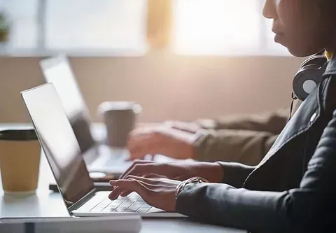 Una mujer está escribiendo en una computadora portátil mientras usa auriculares.