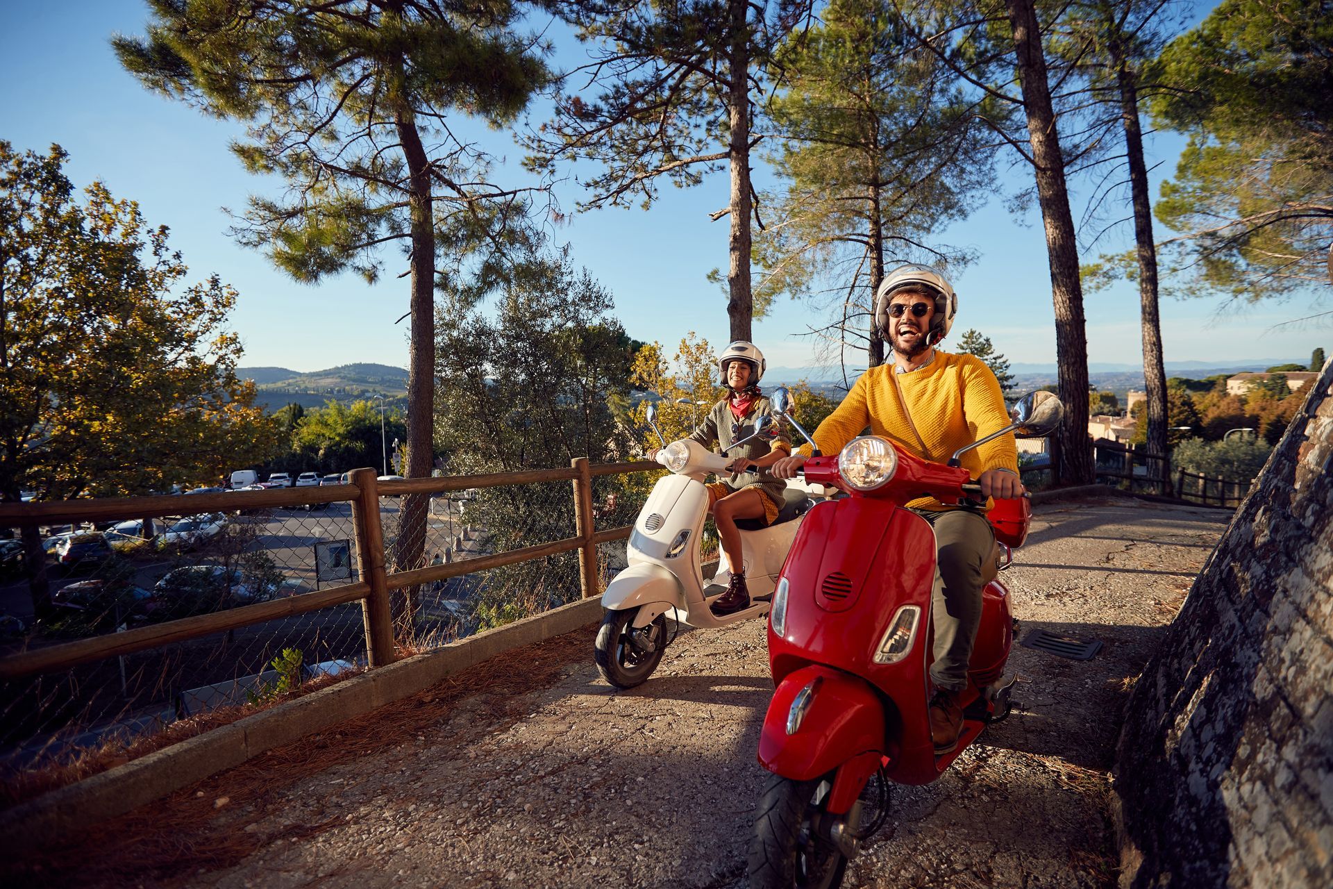 Deux personnes circulent en scooter sur un chemin ensoleillé.
