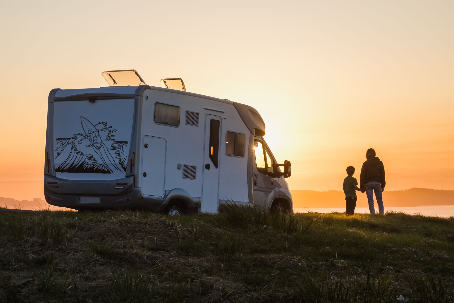Un camping-car avec deux personnes en contre-jour, face au soleil couchant.