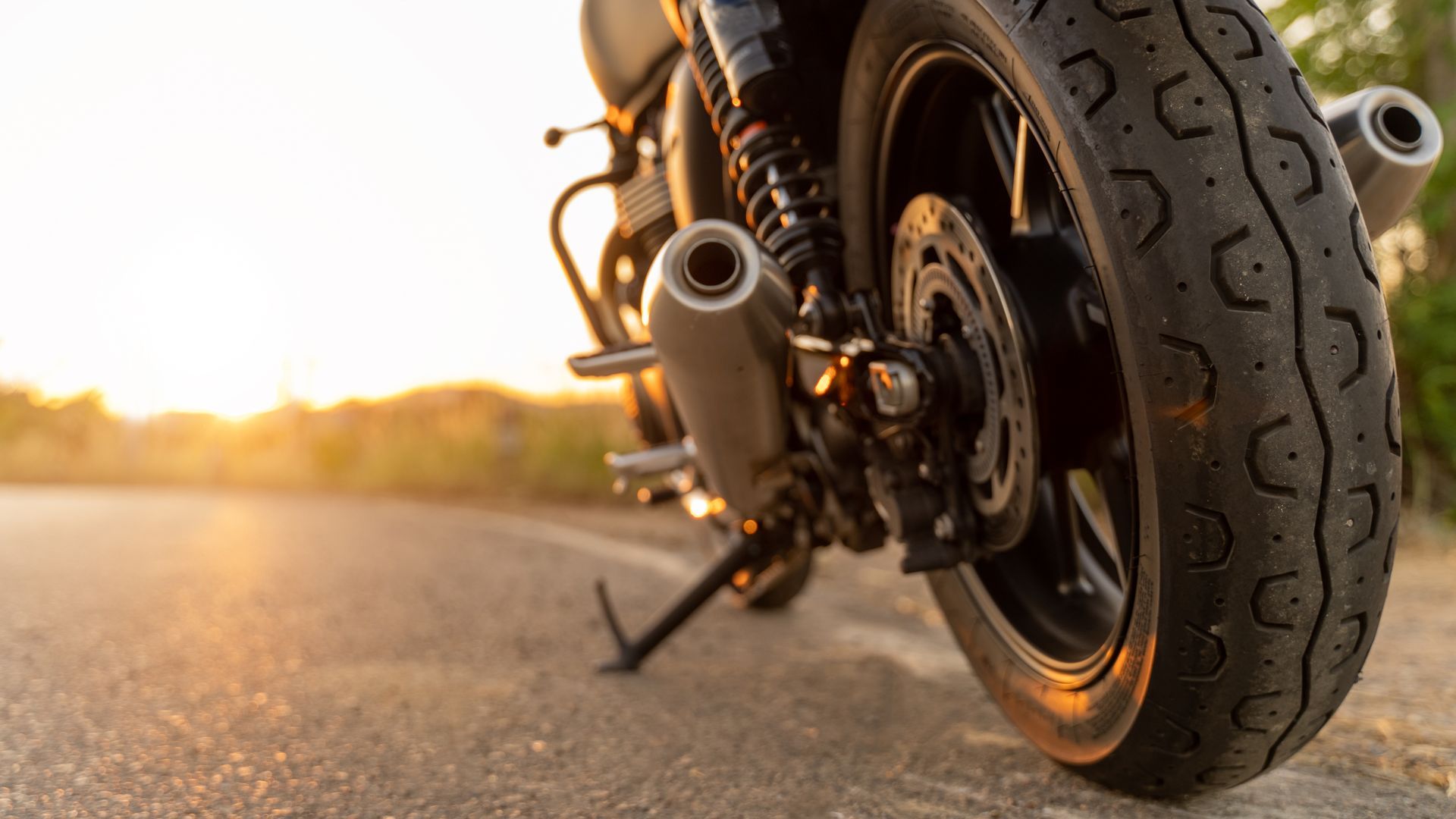 Gros plan sur un pneu de moto sur une route ensoleillée au coucher du soleil.