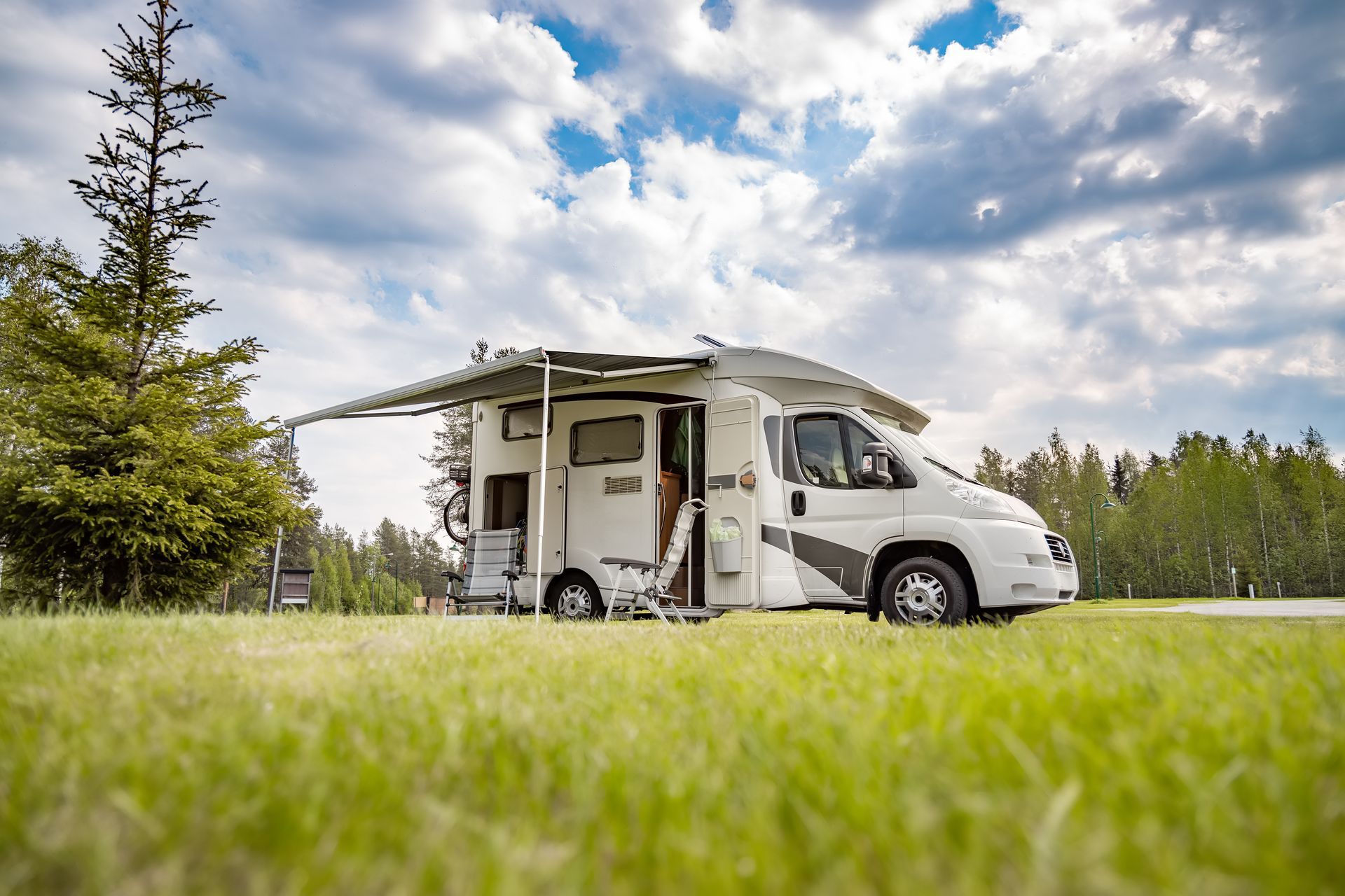 Un camping-car avec auvent, stationné sur un terrain herbeux sous un ciel nuageux.