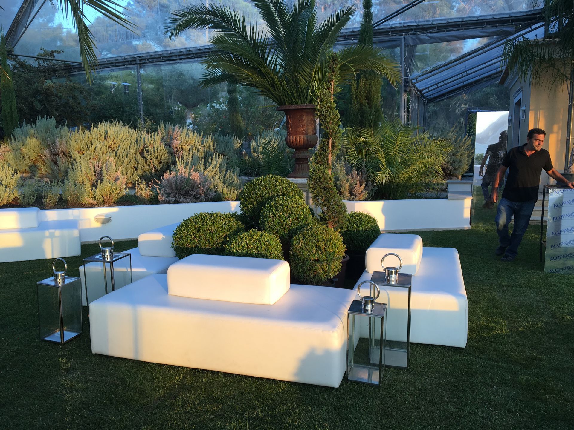 Um homem de camisa preta está parado em um jardim com móveis brancos