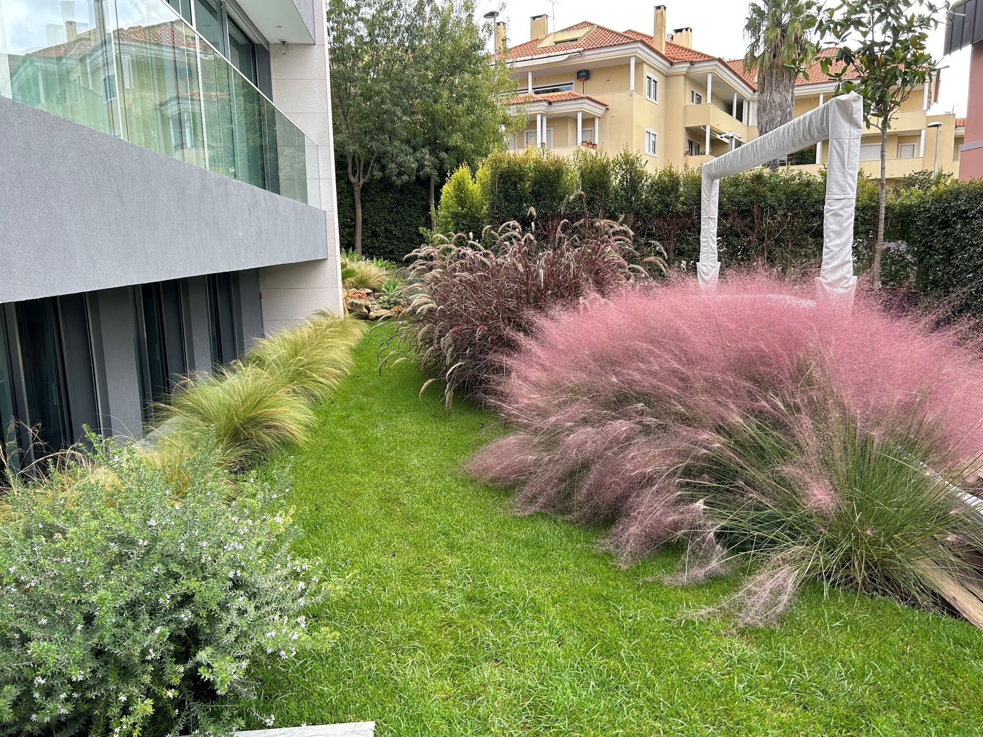 Um gramado verdejante com plantas rosas em frente a um prédio.