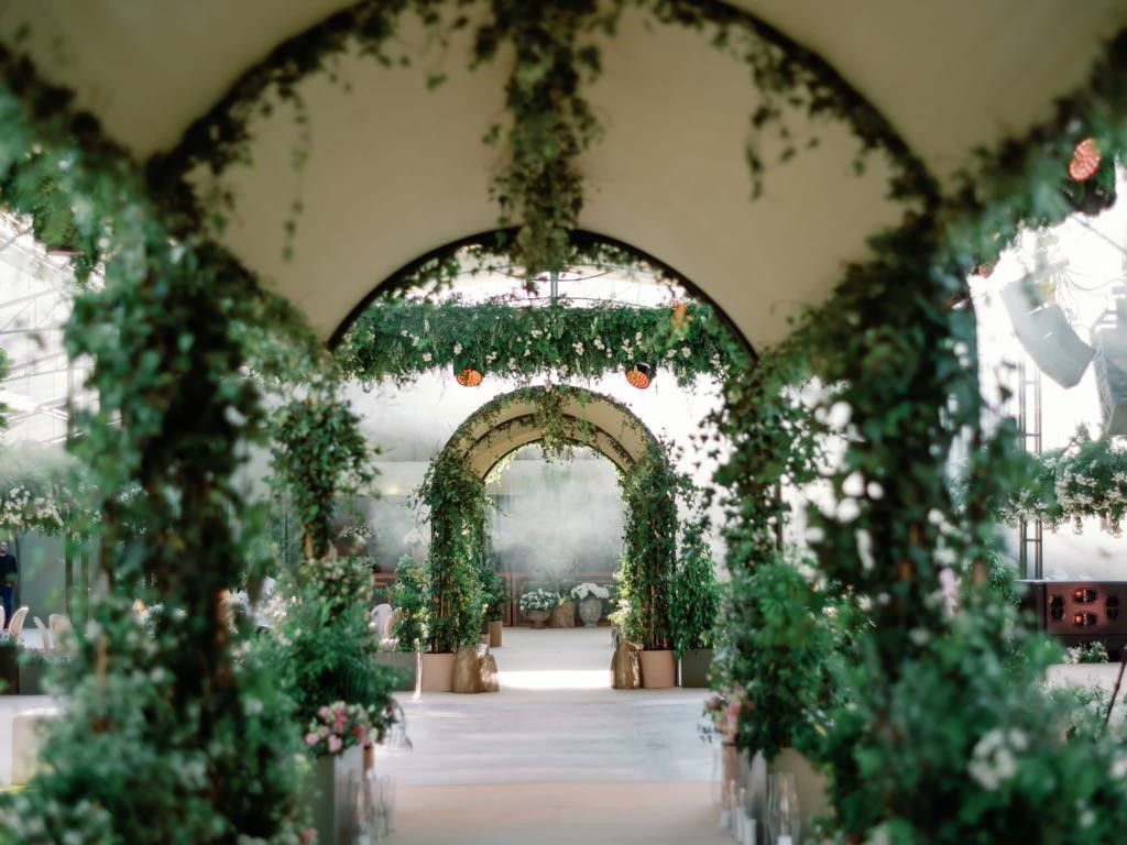 Uma cerimônia de casamento está acontecendo sob um dossel coberto de vegetação.