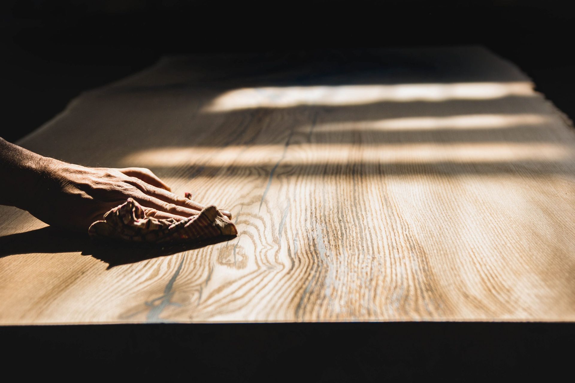 Essuyage à la main d'une surface en bois avec un chiffon, éclairée par la lumière du soleil.