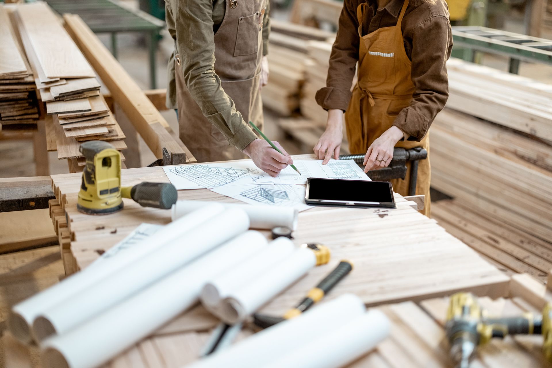 Deux personnes dans un atelier, entourées de bois et d'outils, examinent des plans.