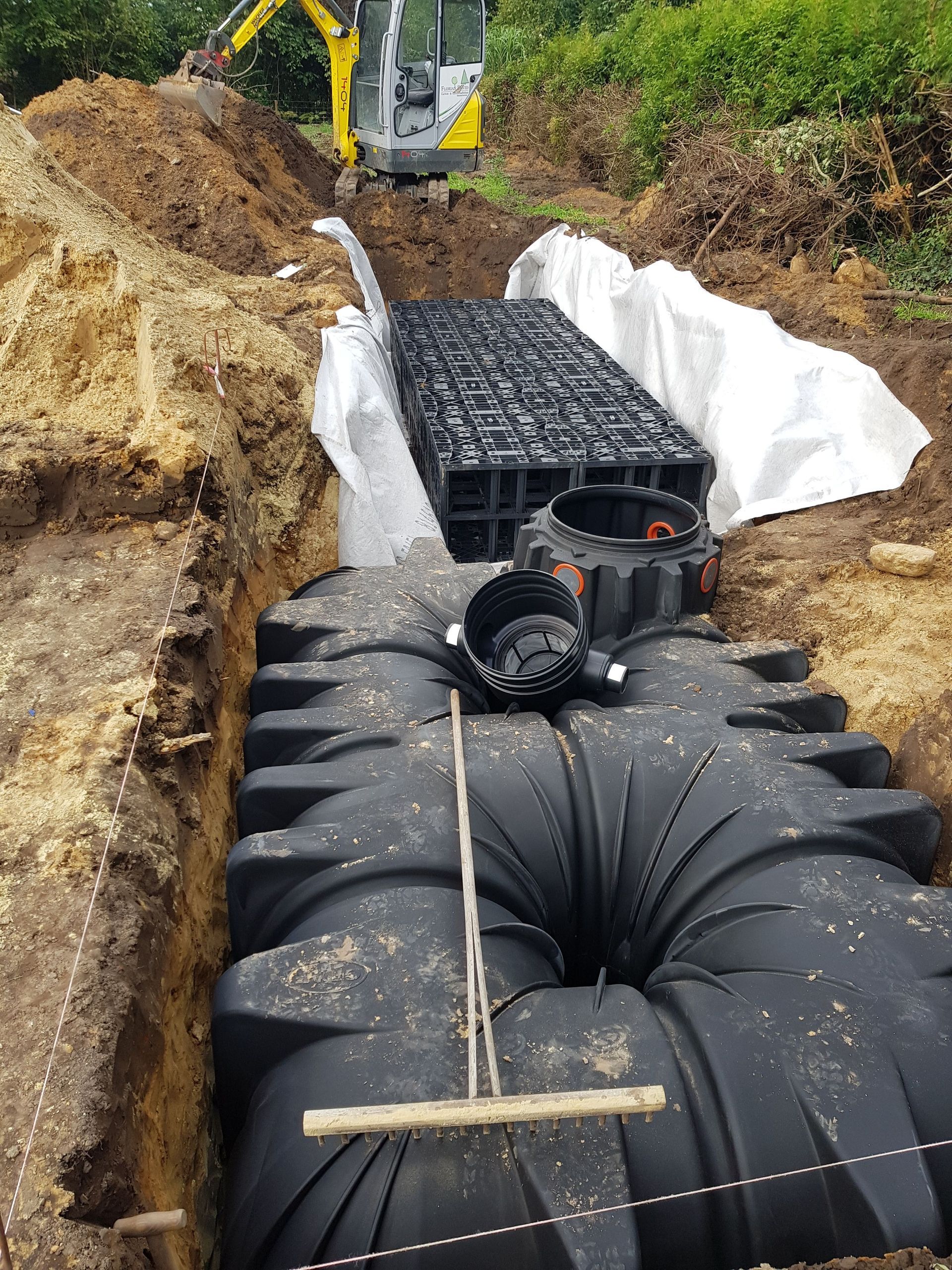 In einem Graben wird ein großes schwarzes Drainagesystem installiert.