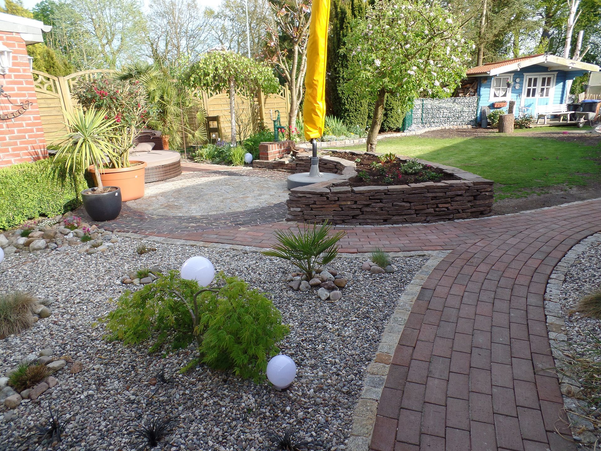 Ein Garten mit einem Ziegelweg und einem gelben Sonnenschirm