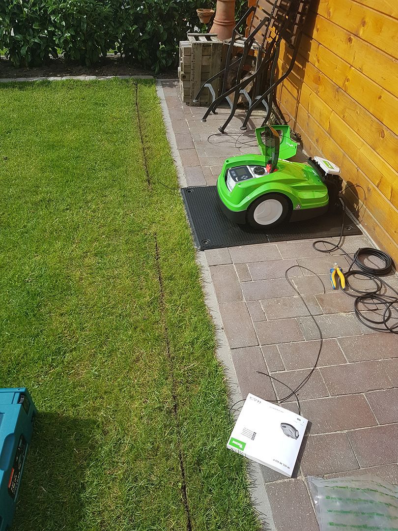 Ein grüner Mähroboter steht auf dem Bürgersteig neben einem Holzgebäude.