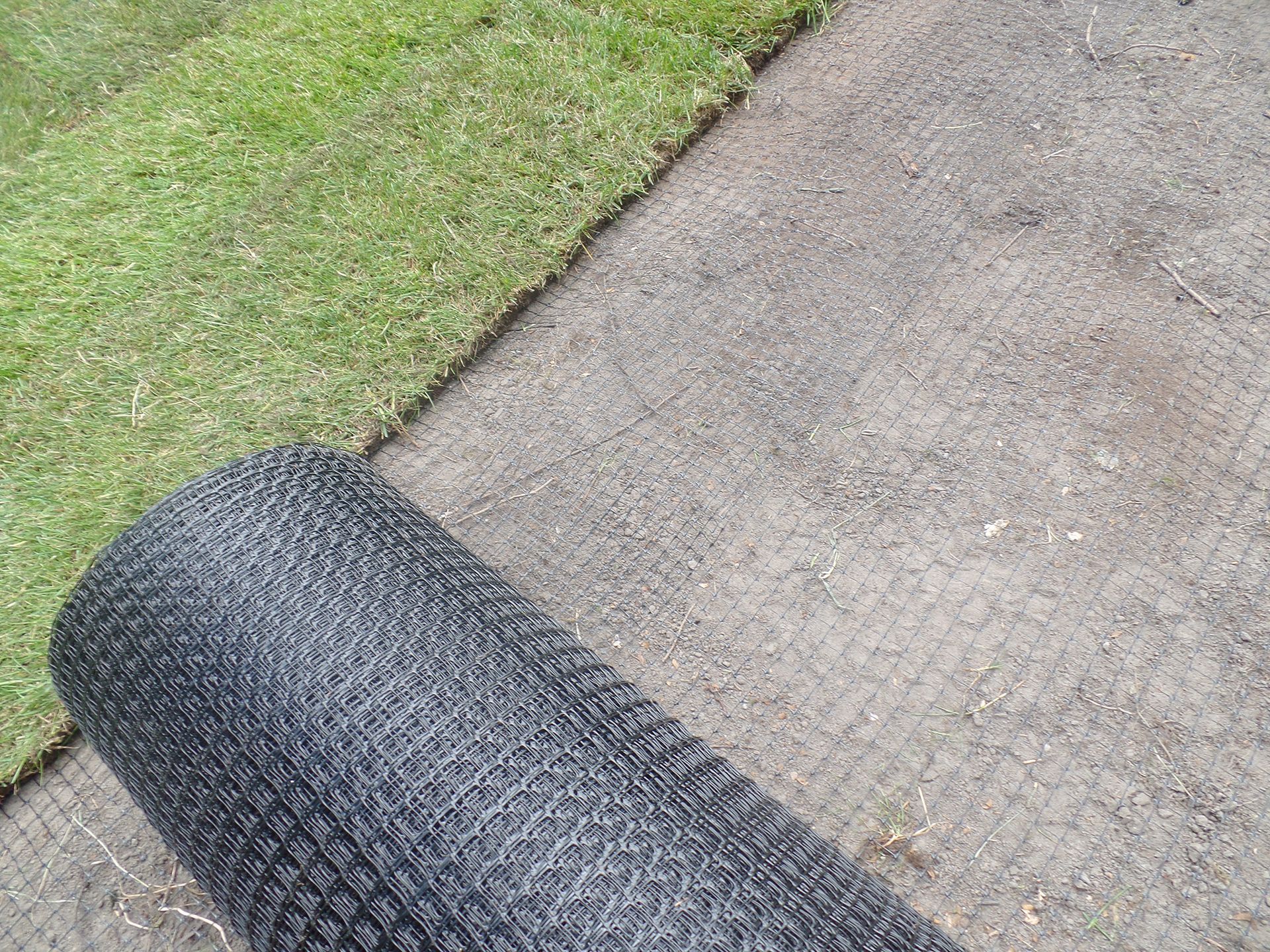 Eine Rolle schwarzen Zauns liegt auf einem Gehweg neben einem Rasen.