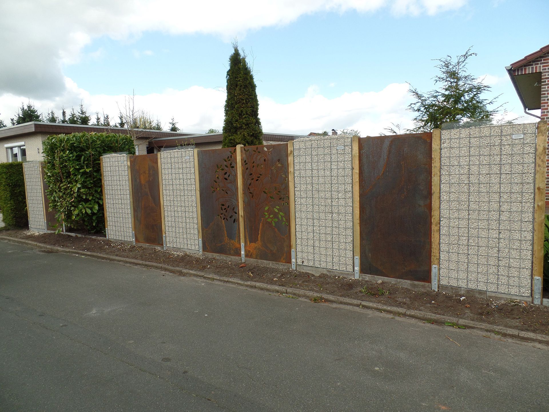 Entlang einer Straße steht ein Zaun aus Stein und Metall.