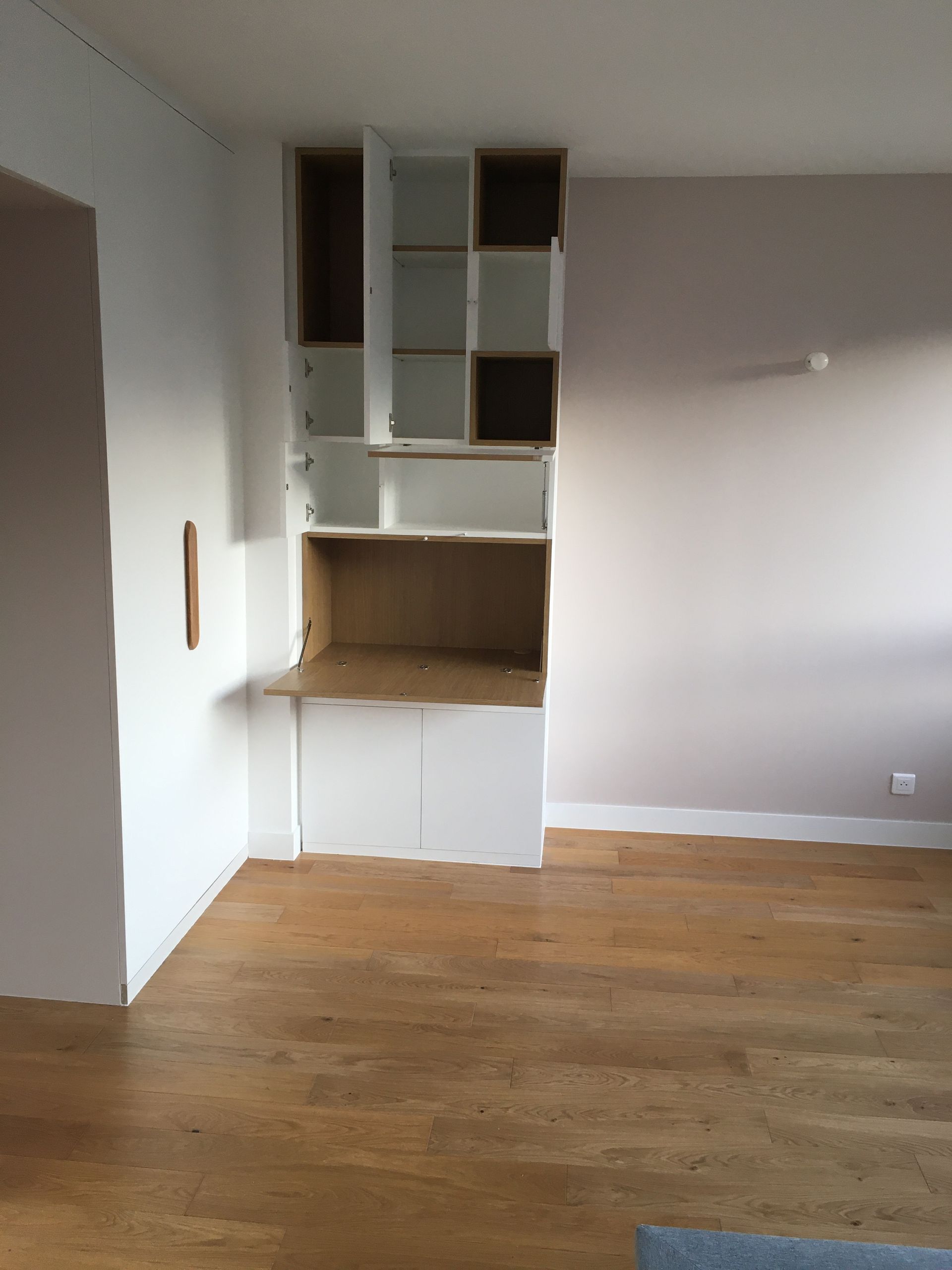 Étagères en bois encastrées sur des murs blancs et beiges dans une pièce avec parquet.