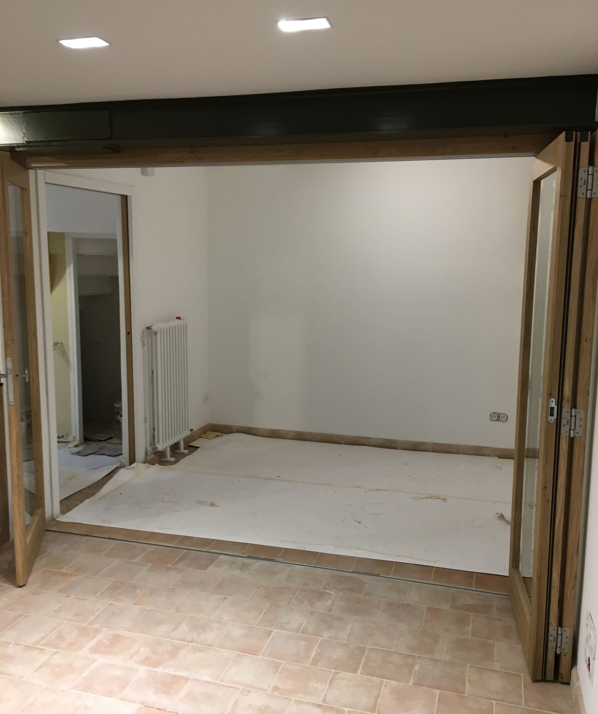 Pièce intérieure avec portes pliantes ouvertes, murs blancs et une porte visible donnant sur un autre espace.