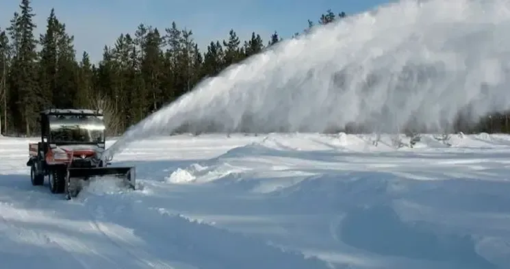 Eine Schneefräse bläst Schnee auf ein schneebedecktes Feld.