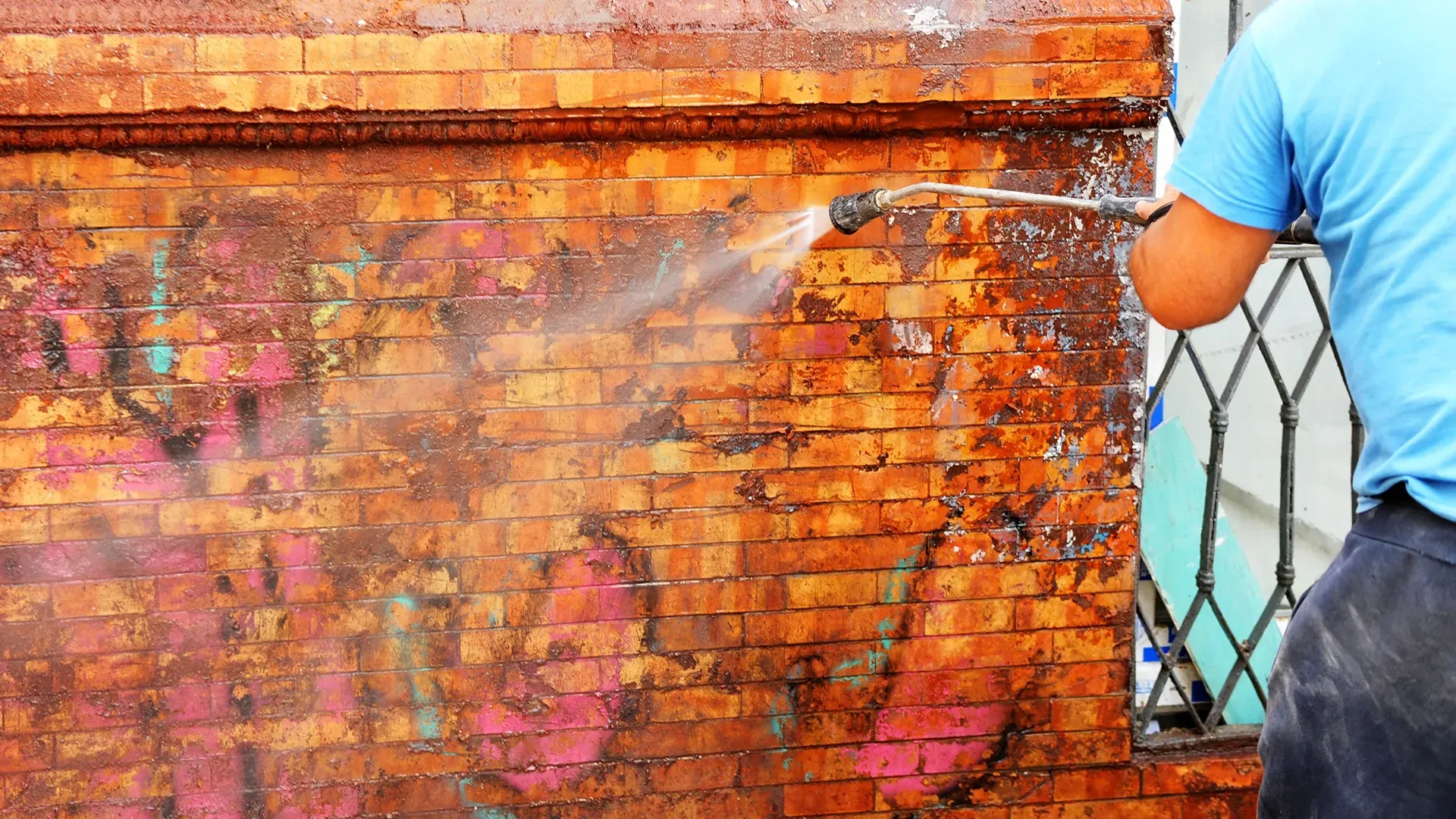 Persona limpiando los grafitis de la pared de ladrillos de la calle