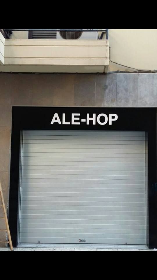 La fachada de una tienda ALE-HOP con una persiana de seguridad metálica gris cerrada bajo un letrero negro.