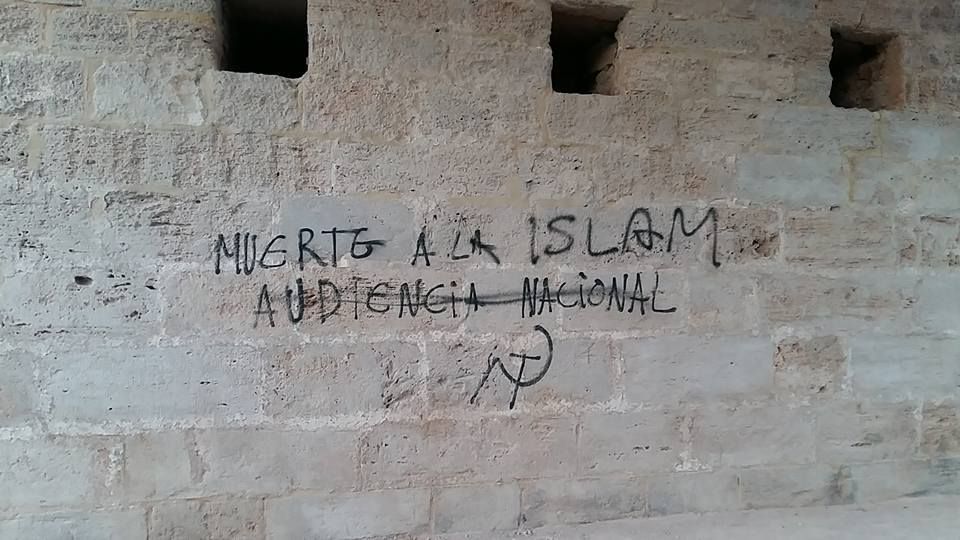 Un muro de piedra con grafitis pintados con aerosol negro que dicen 