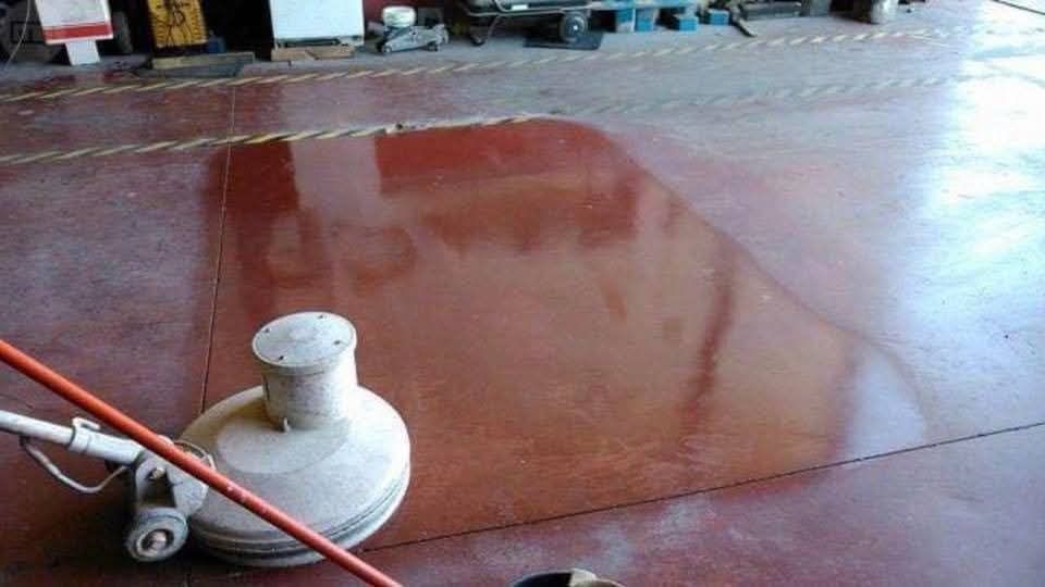Una pulidora de suelos sobre el suelo rojo oscuro de un almacén, mostrando una sección pulida que ha limpiado recientemente.