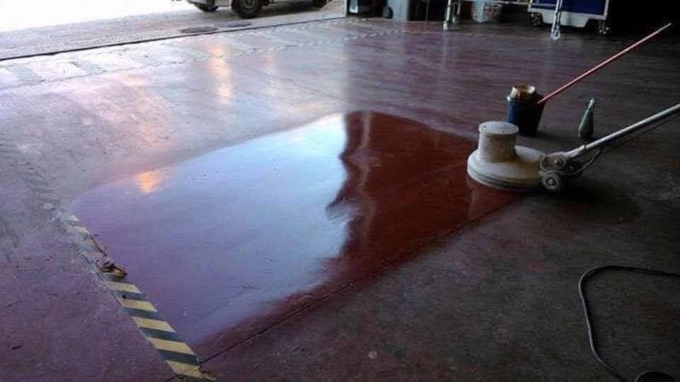 Una pulidora de suelos trabaja sobre una superficie de hormigón rojo, creando una zona brillante y reflectante que contrasta con el acabado mate del suelo.