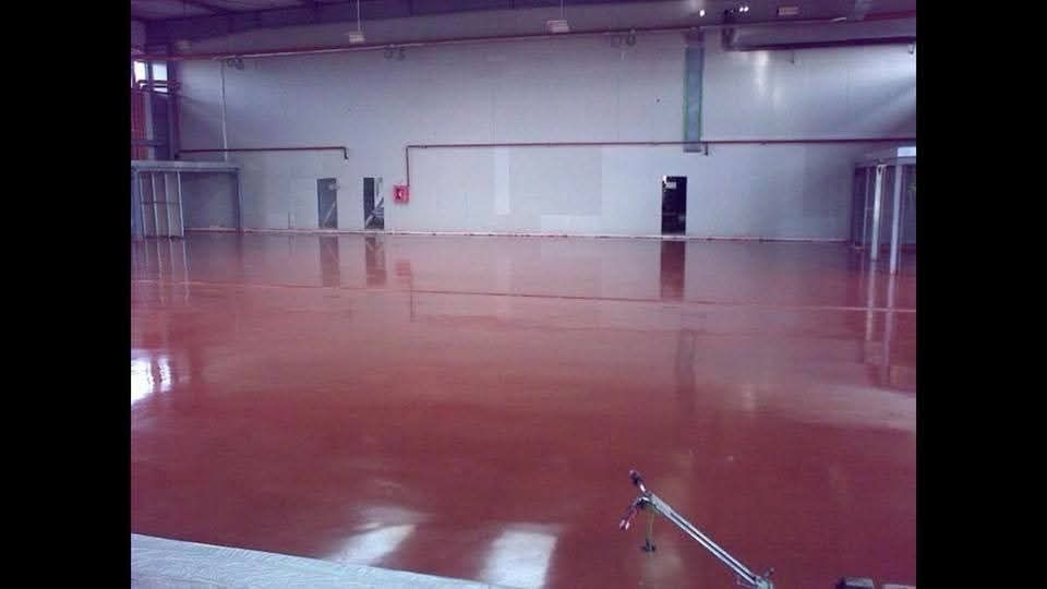 Un almacén amplio y vacío, con techos altos y un suelo de resina epoxi brillante de color rojo oscuro.