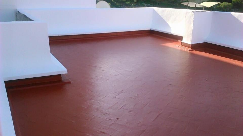 Una azotea plana con una capa impermeabilizante de color marrón rojizo uniforme recién aplicada, bordeada por paredes blancas impolutas.