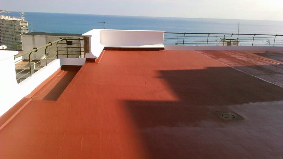 Una terraza plana pintada de rojo en la azotea, con vistas al océano en un día soleado y luminoso.