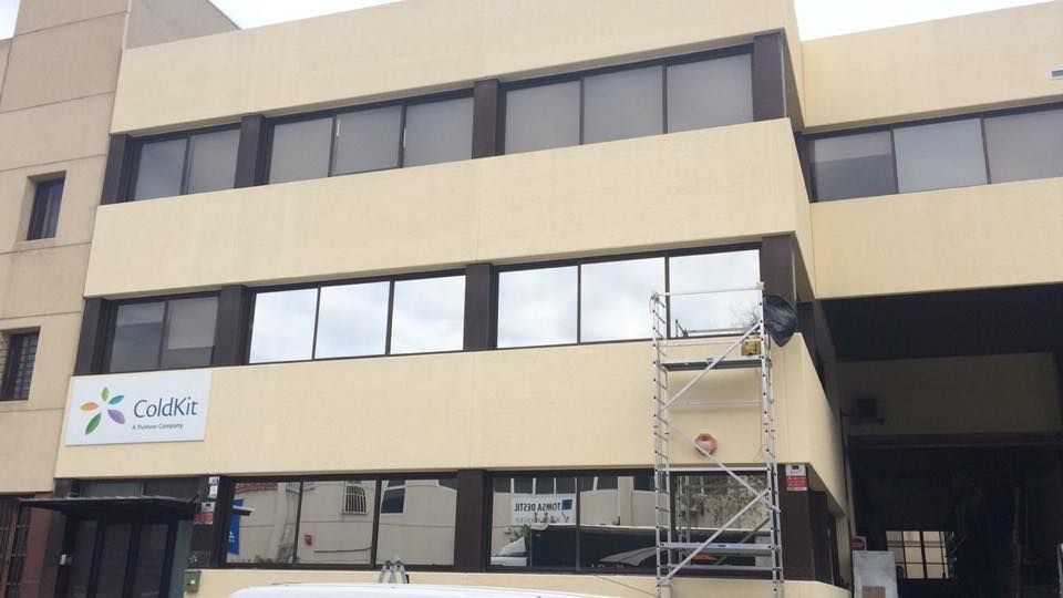 Un edificio comercial de tres plantas, de color beige, con ventanas horizontales, un letrero de Gold's y andamios metálicos.