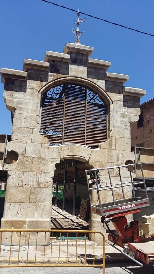 Una estructura de arco de piedra en proceso de construcción exterior, con un tejado escalonado y andamios a la derecha.
