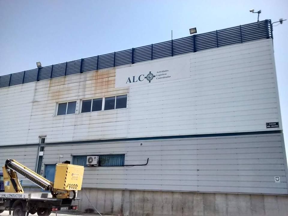 Una plataforma elevadora amarilla estaba estacionada frente a un almacén con paneles metálicos blancos que lucía el logotipo de la empresa ALC.