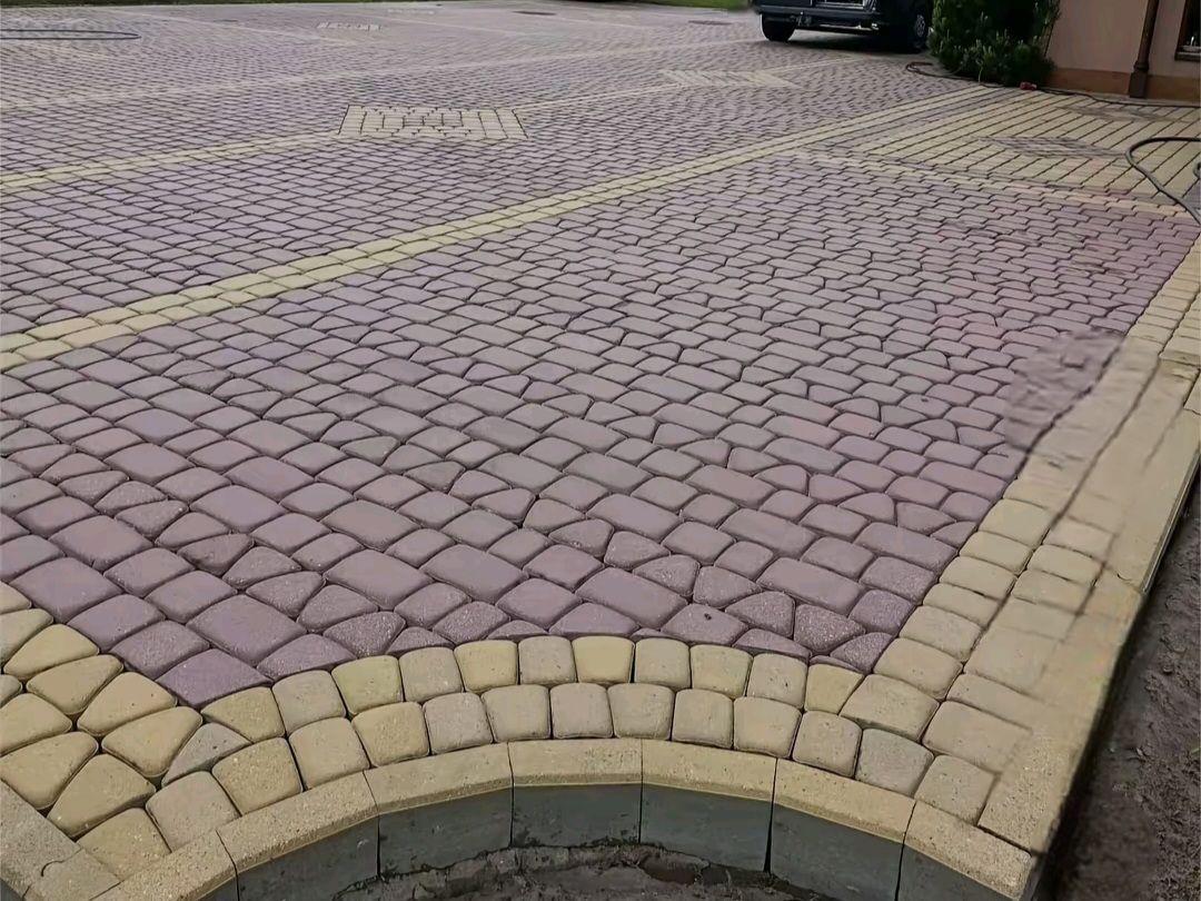 Un camino de entrada pavimentado con adoquines rojos bordeado y dividido por losas rectangulares decorativas amarillas con un diseño curvo.