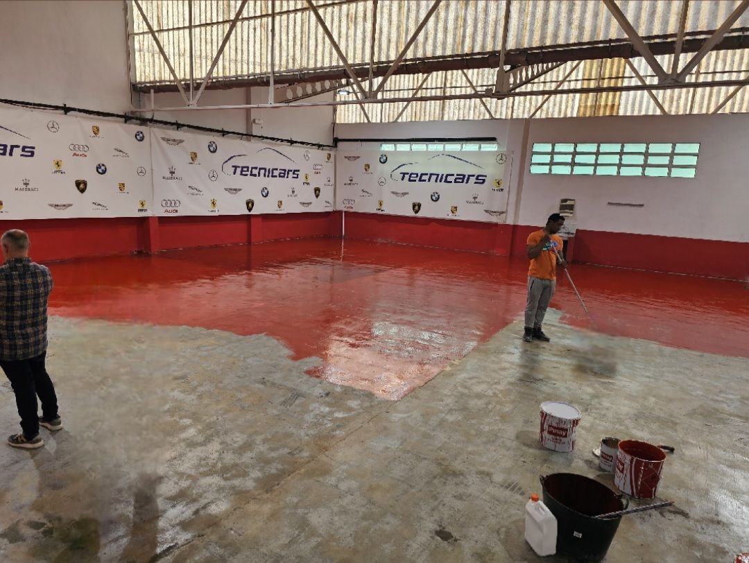Hombre con camiseta naranja pintando suelo de la nave con una brocha
