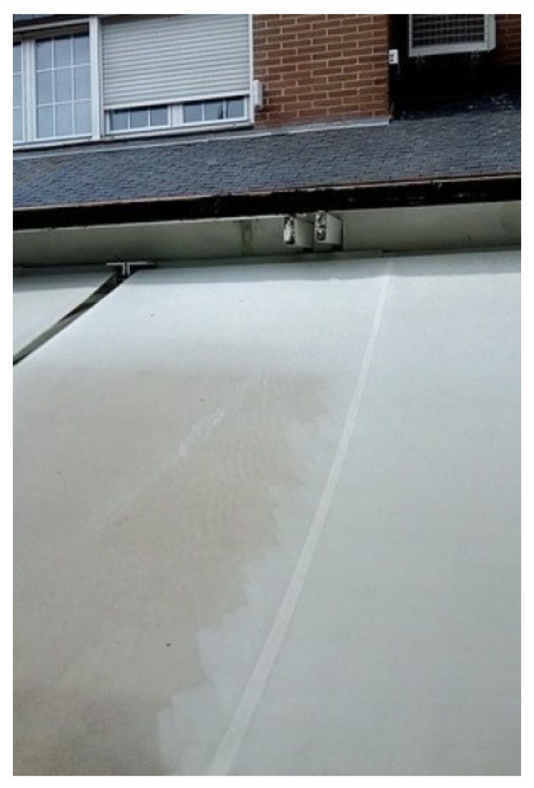Dos paneles solares térmicos blancos instalados en un tejado inclinado bajo la pared de un edificio de ladrillo.