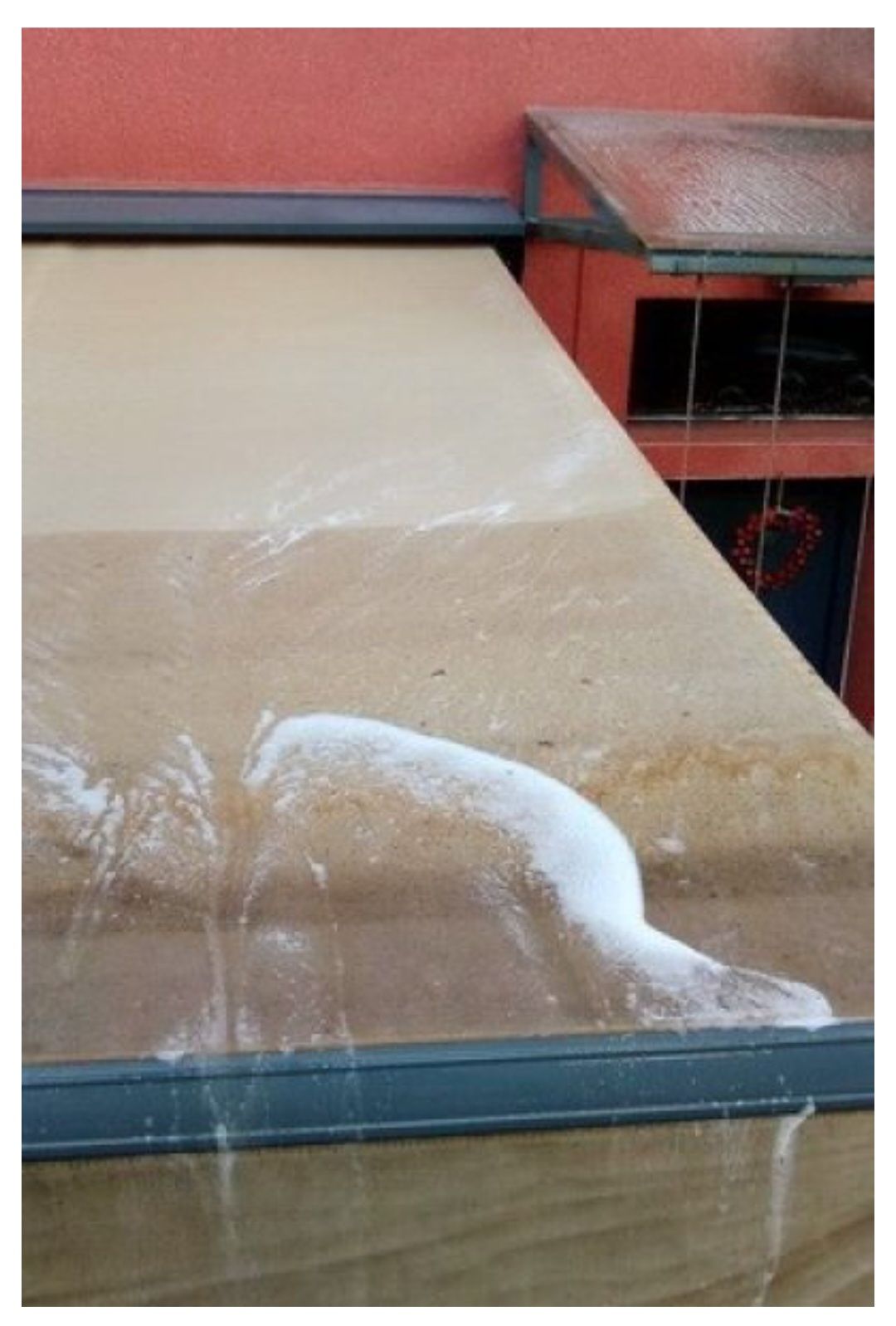 Un toldo exterior de color beige con vetas de residuos blancos o excrementos de pájaros, situado junto a una pared exterior roja.